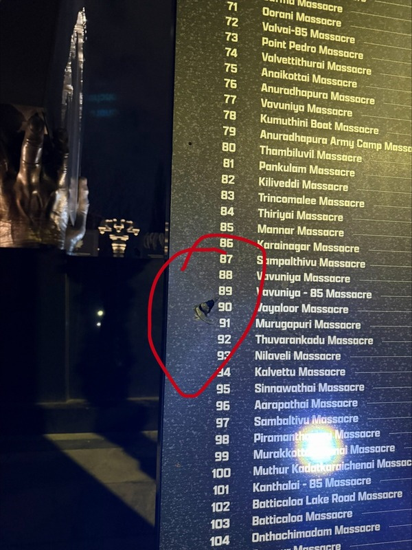 Close-up of vandalized informational panels at the Tamil Genocide Monument, showing red graffiti marks defacing the memorial text